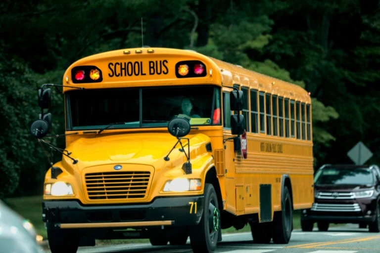 Yellow school bus driving on a road with trees in the background.